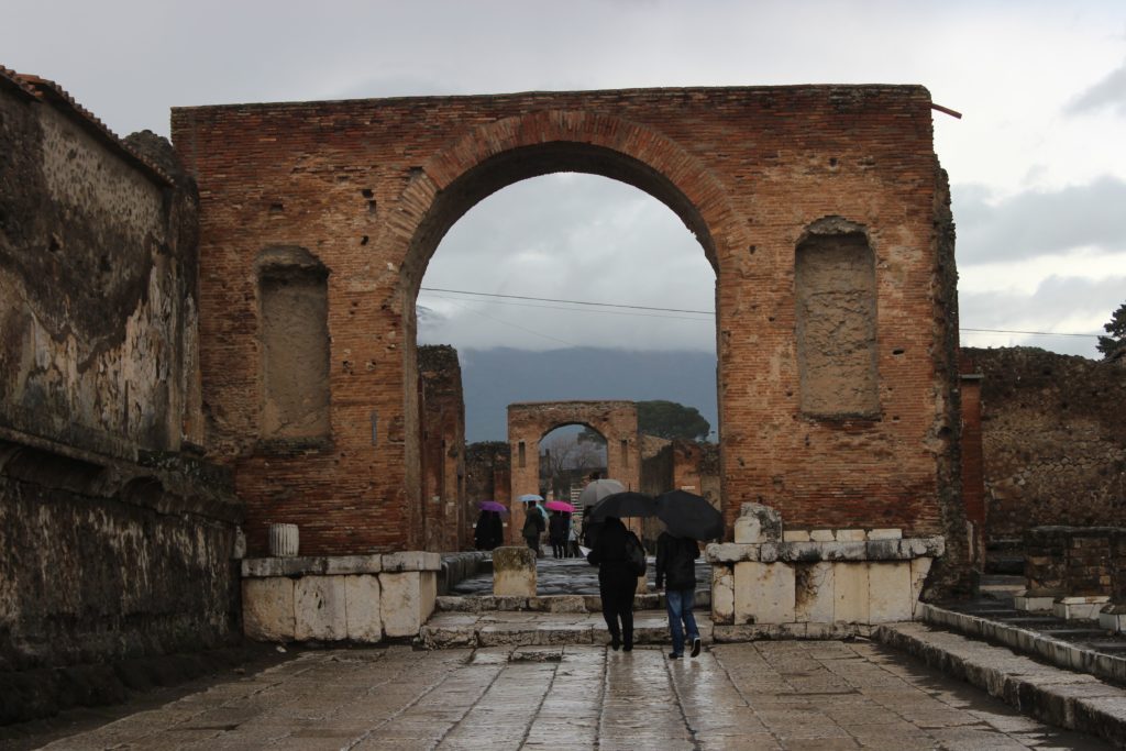 arch of entrance in pompeii with two people with umbrellas