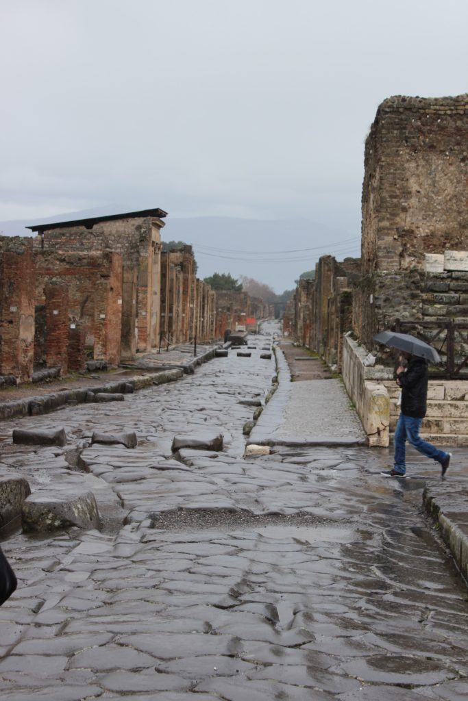 woman crossing pompeii with umbrella while raining