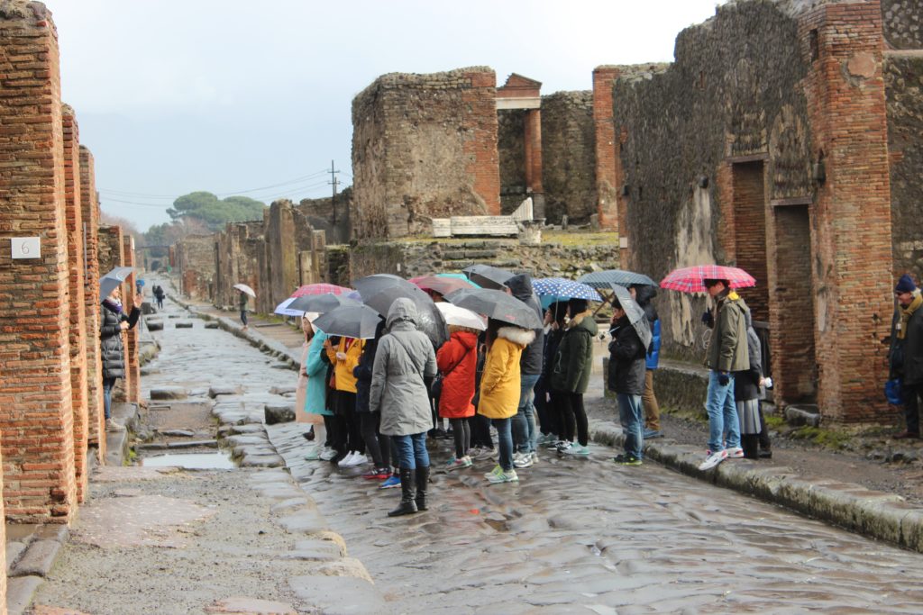 group of tourists with umbrellas on a tour in pompeii
