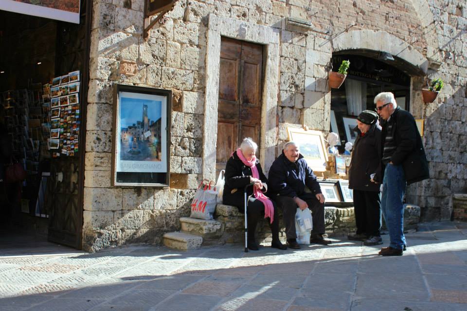 elderly italians sitting on a bench on the streets of san gimignano