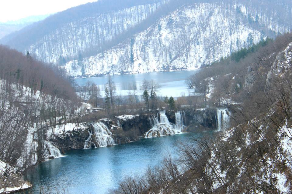 winter wanderland at plitvice lakes with mountains covered in snow, frozen waterfalls and fronzen lake