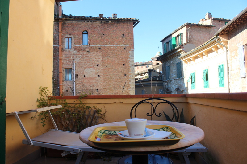 balcony with a chair, a cappuccino on the table, surrounded by pastel typical italian buildings in siena